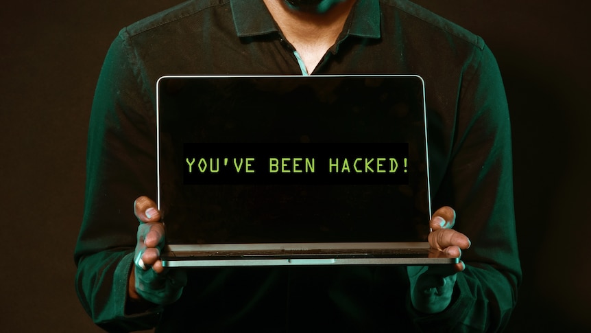 A man holding a laptop, on the screen it reads 'You've been hacked!'
