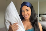 Tahnee Jash is smiling holding a pillow in her left hand and wearing a dark blue sleeping mask around her forehead
