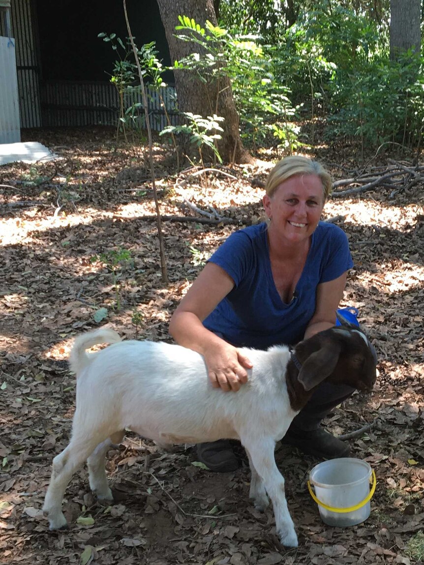 Woman smiling kneeling in a paddock with two goats