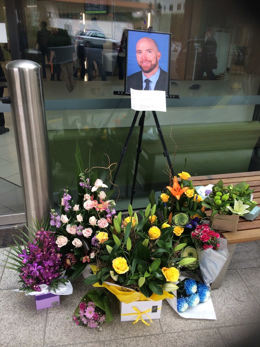 Flowers are placed under a photo of Patrick Pritzwald-Stegmann outside the entrance to Box Hill Hospital.