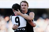 Two Port Adelaide AFL players embrace as they celebrate a win.