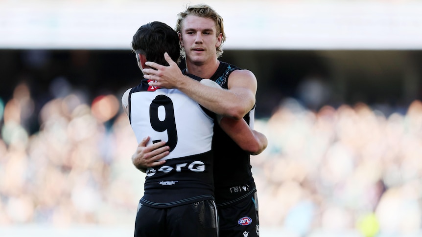 Two Port Adelaide AFL players embrace as they celebrate a win.