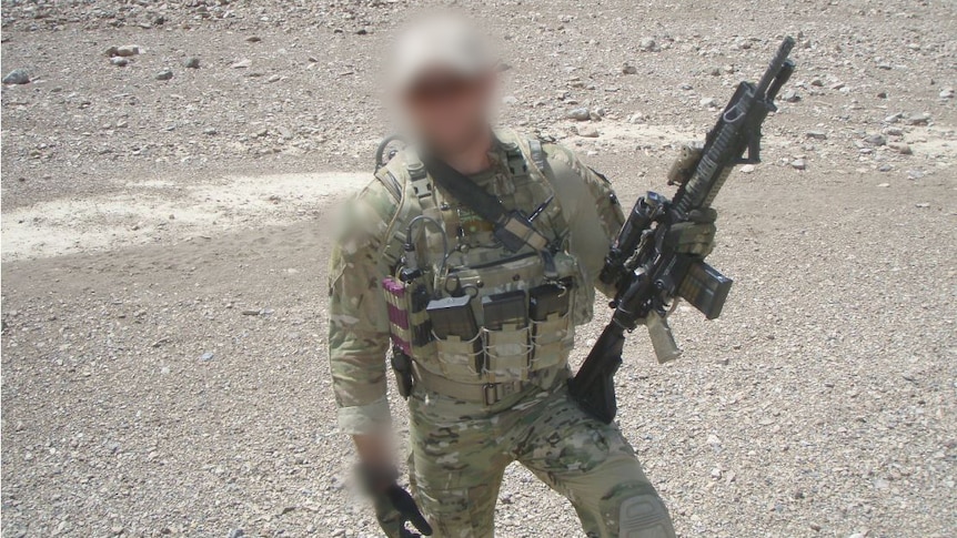 A soldier standing in a desert, holding a rifle, with a blurred face.