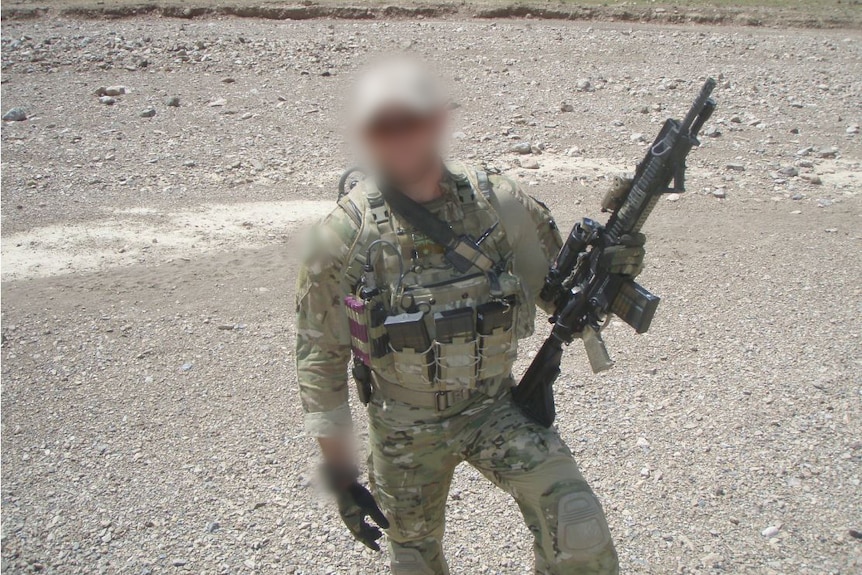A soldier standing in a desert, holding a rifle, with a blurred face.