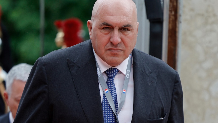 A heavily built, unsmiling man wearing a suit and tie. 