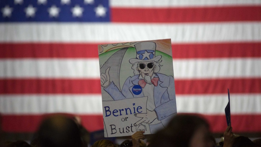 A man holds up a sign with a cartoon drawing saying 'Bernie or Bust'.