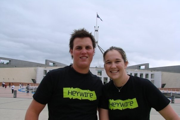Man and woman wearing Heywire t-shirts standing in front of Parliament House in Canberra.