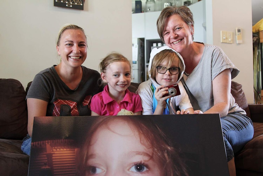 two mothers with their two children holding a huge photograph