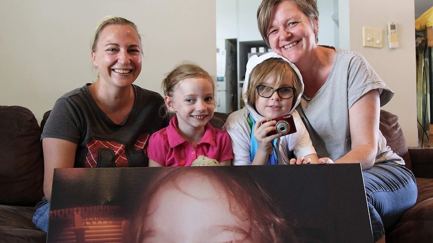 two mothers with their two children holding a huge photograph