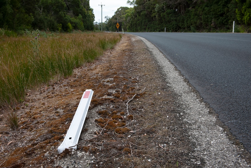 White roadside marker knocked down beside a road. 