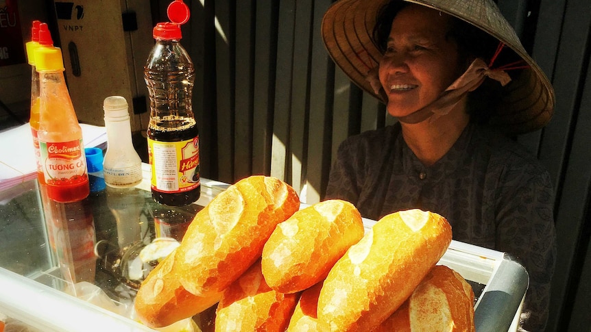 Woman sits behind cabinet in Vietnamese street stall with bred rolls on top of cabinet