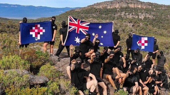 A group of around 20 men, dressed in black and wearing masks, holding neo-Nazi flags and the Australian flag in The Grampians