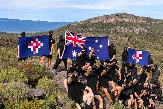 A group of around 20 men, dressed in black and wearing masks, holding neo-Nazi flags and the Australian flag in The Grampians