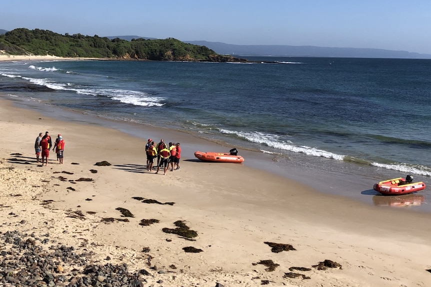 Two groups of lifesavers stand on a beach, with two rescue dinghies sitting on the tideline.