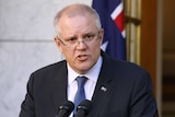 Scott Morrison looks over the top of his glasses as a speaks with an Australian flag behind him