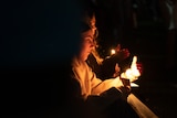 Two women hold candles in darkness.
