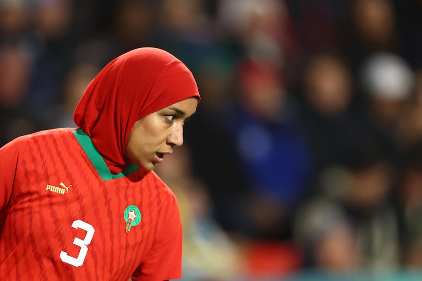 Nouhaila Benzina dressed in red wearing a hijab on the soccer pitch for Morocco.