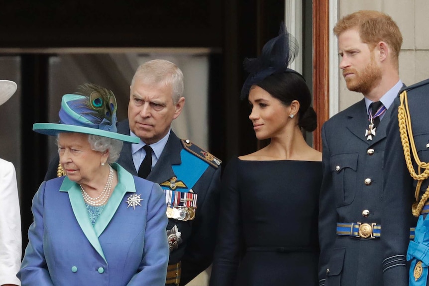 Queen Elizabeth II, Prince Andrew, Meghan Markle, Prince Harry stand together and look to the the left of screen