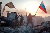 Wagner Group military company members wave a Russian national and Wagner flag atop a damaged building in Bakhmut.