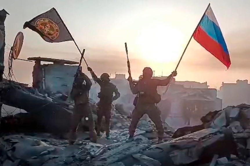 Wagner Group military company members wave a Russian national and Wagner flag atop a damaged building in Bakhmut.