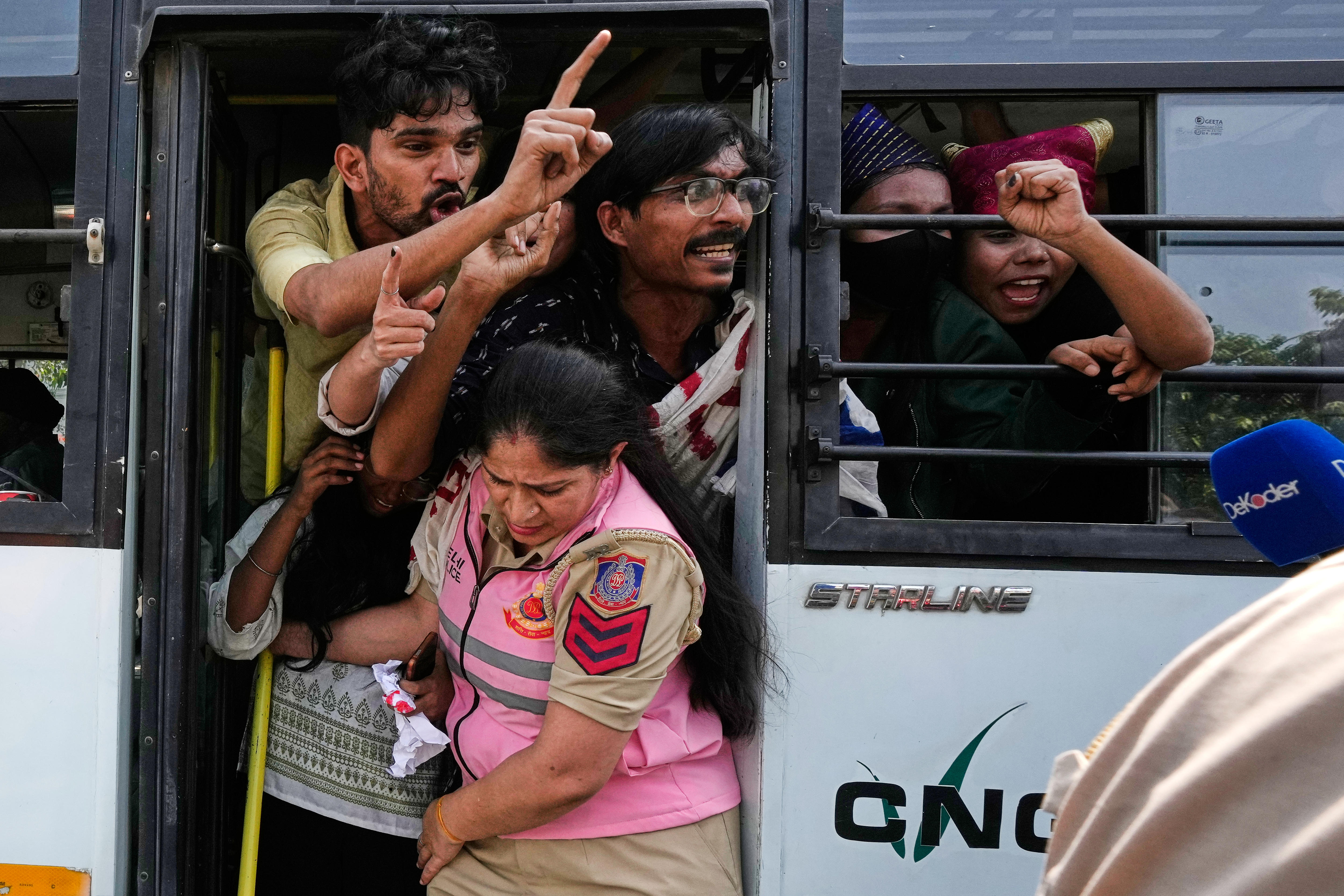 A police officer tries to hold protesters inside a police vehicle with an open side door