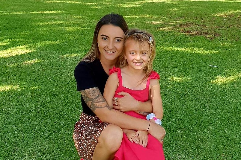 A Mum and her daughter smile at the camera in a park.