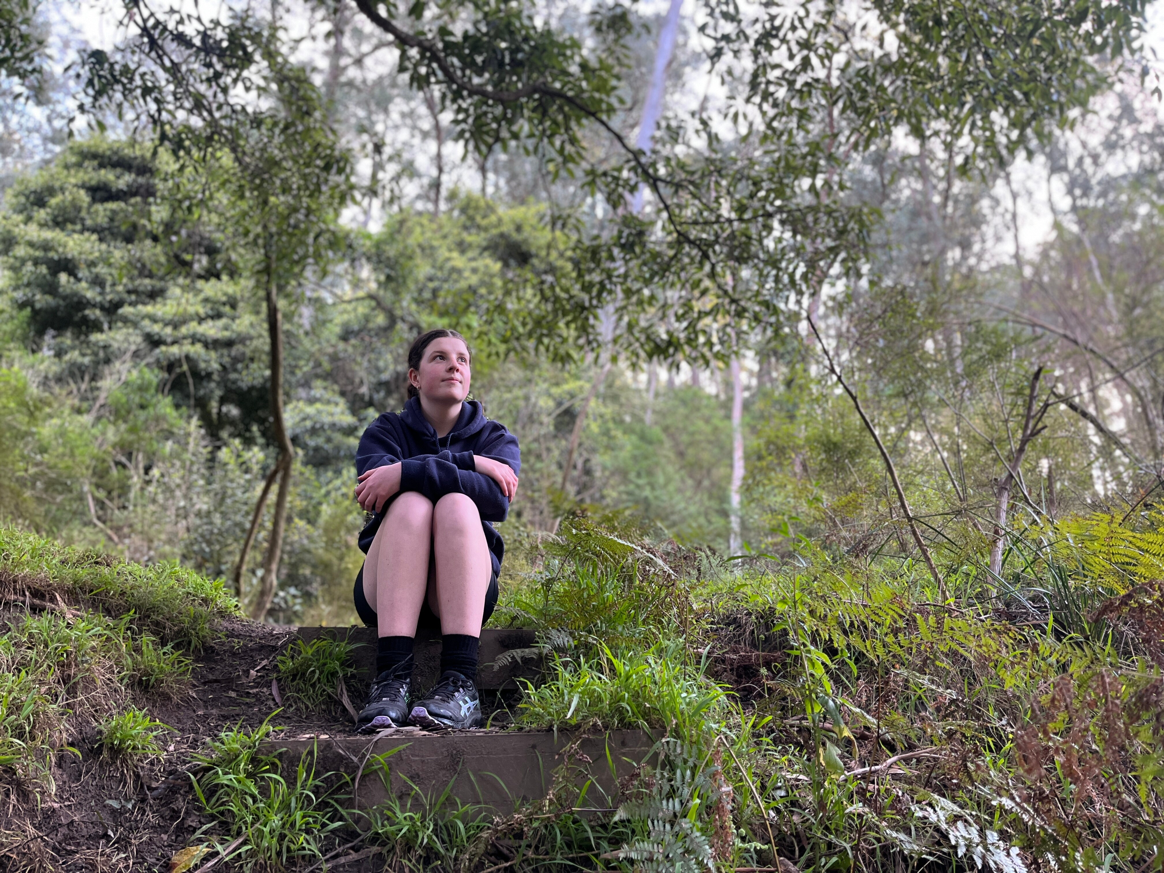 A young woman sitting on a rock step in the forest
