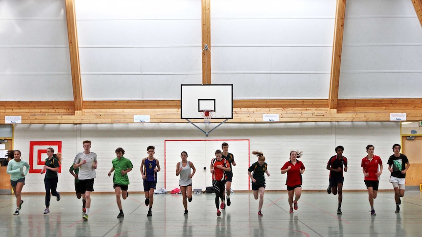 A line of students running across a basketball court