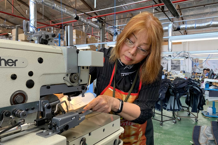 Nga Huynh, a woman with red hair and glasses, sews clothes on a machine.