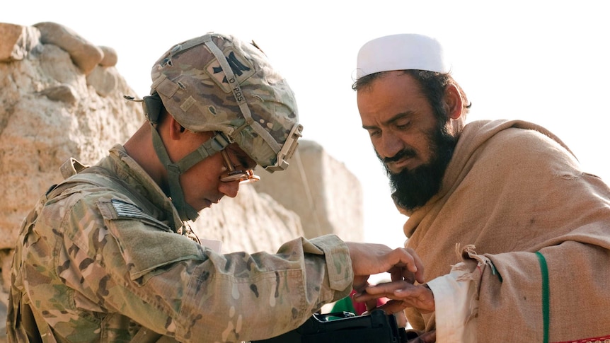 US soldier Mark Domingo fingerprints a man in traditional Afghan attire.