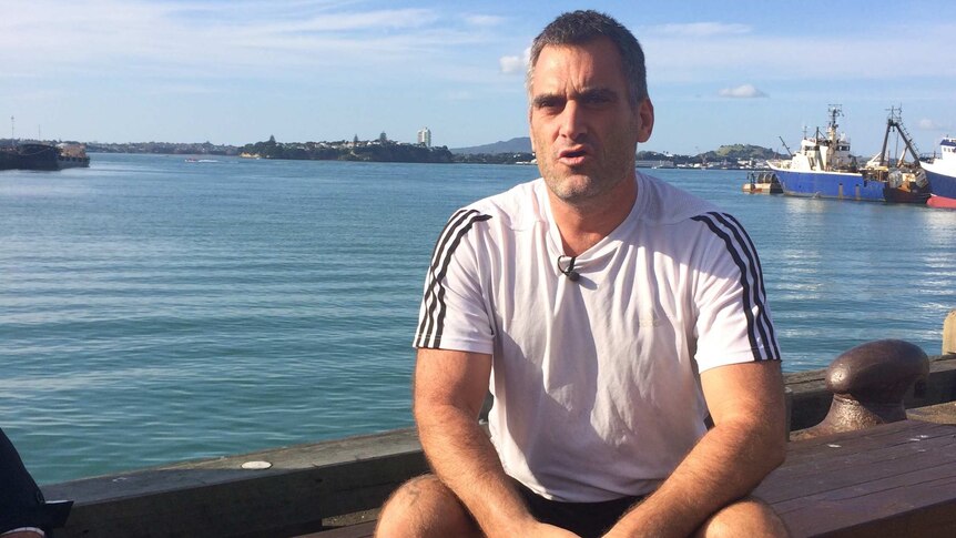 Shaun Wynyard sits in front of a wharf.