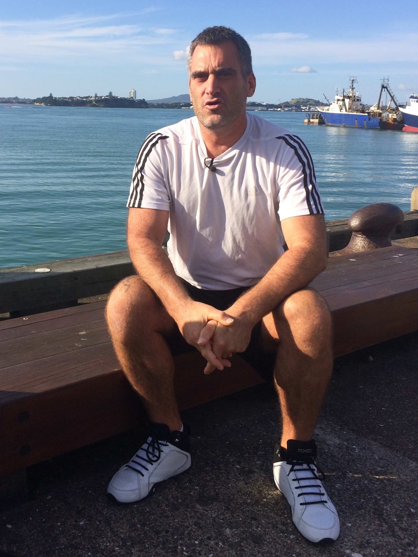 Shaun Wynyard sits in front of a wharf.