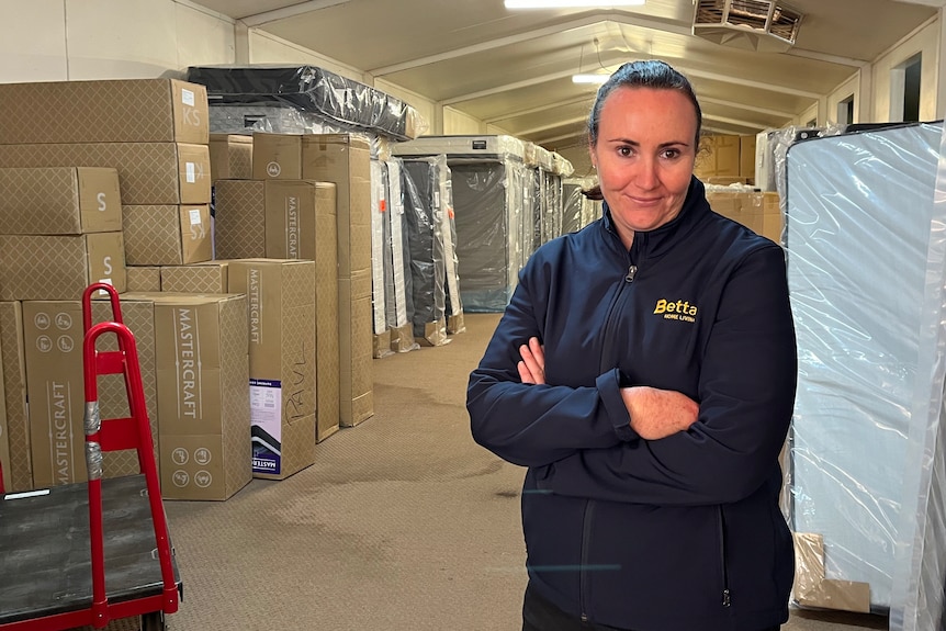 A woman in a blue puffer jacket stands inside of a shed full of stock