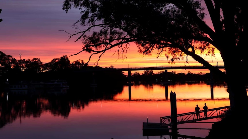 Sunset over the Murray River with trees, a bridge and two people watching