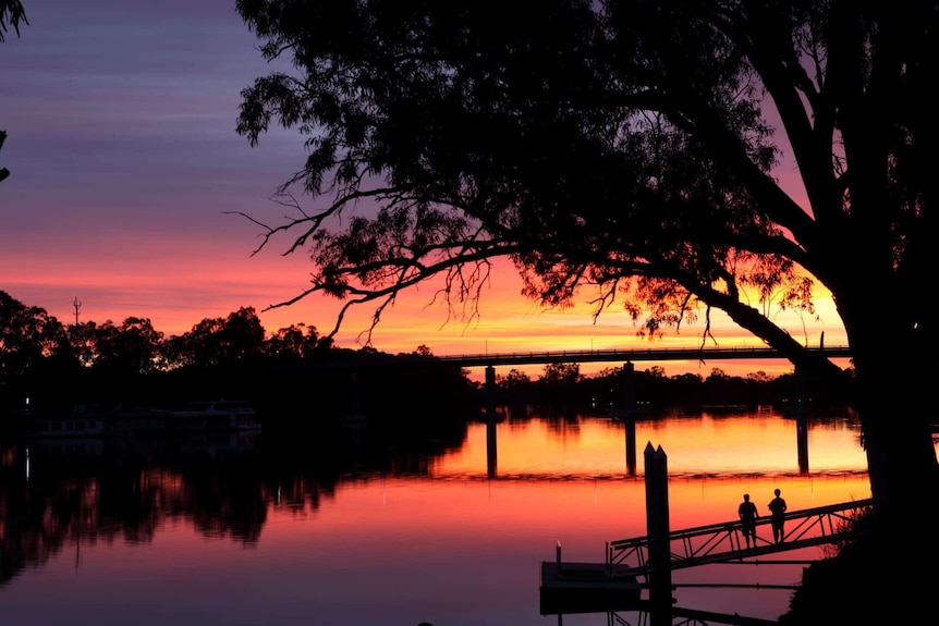 Sunset over the Murray River with trees, a bridge and two people watching