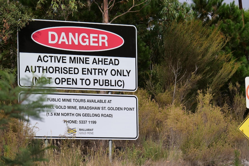 Un cartel de pie en matorral advirtiendo de los peligros relacionados con una mina más adelante