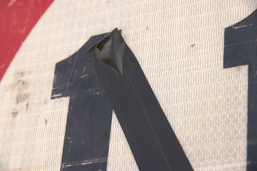 Extreme close-up of a black piece of tape on the top of the number one on a speed limit sign.