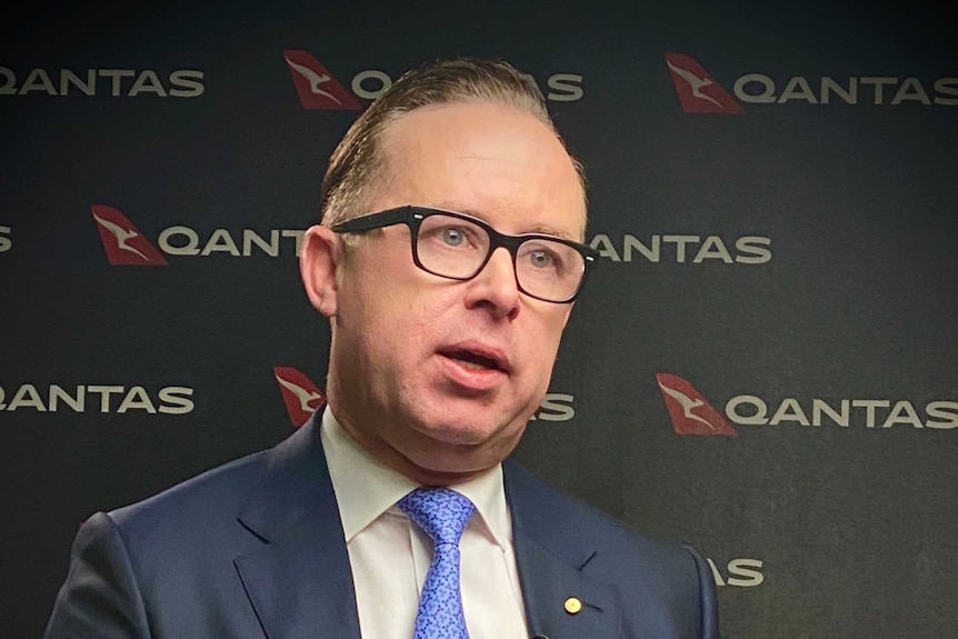 Alan Joyce seated, gesturing his hands, with Qantas logos behind him.