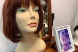 A wig on model next to a framed photo of an older woman