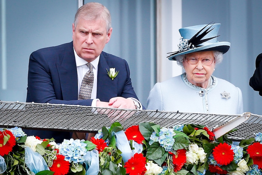 Prince Andrew and Queen Elizabeth looking serious as they stand at a balcony decorated with flowers