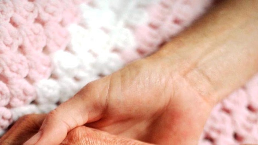 An elderly person's hand is held by a younger person's hands.