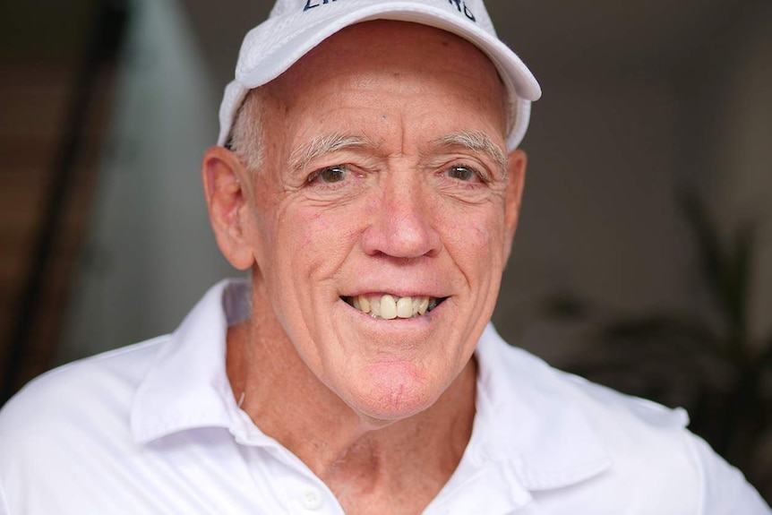 Older man white shirt on and and white cap smiling at the camera