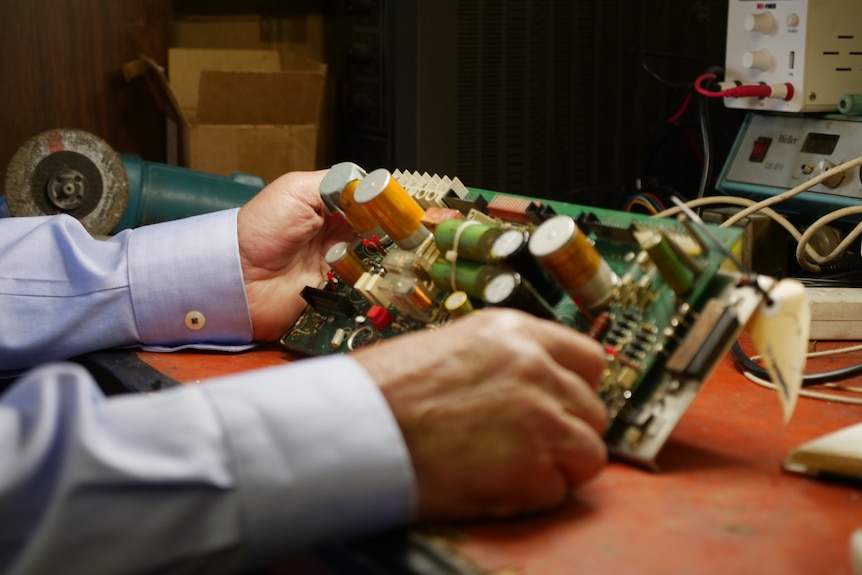 A close up of two hands holding a board with a number of electrical wires and components.