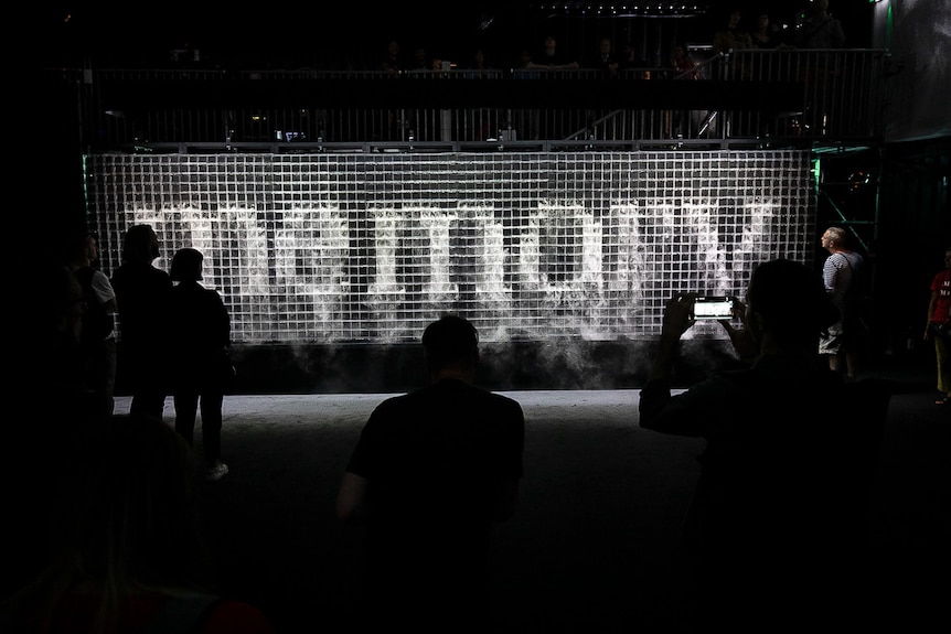 The word 'memory' is spelled out in billowing clouds of water vapour on a gridded wall in a gallery.
