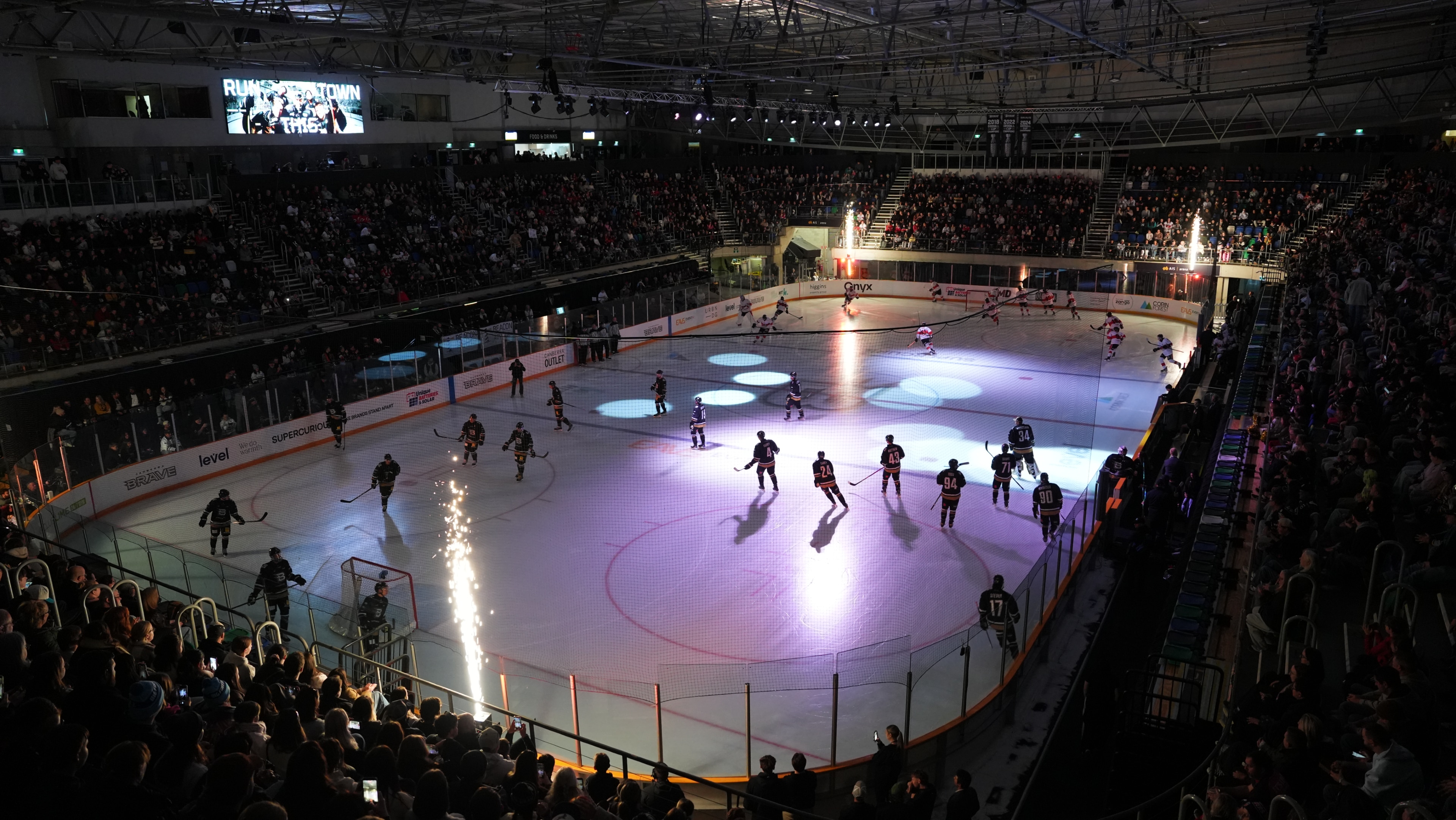People play ice hockey on a rink in a darkened stadium.