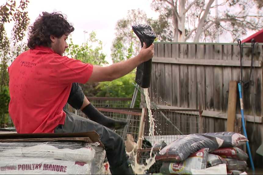 Water pours out of the gumboot of a worker who sits on stacked packets of manure.