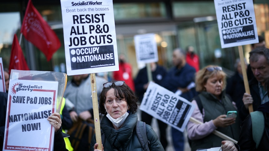 woman stands in front of protest crowd holding sign reading resist all P&O job cuts