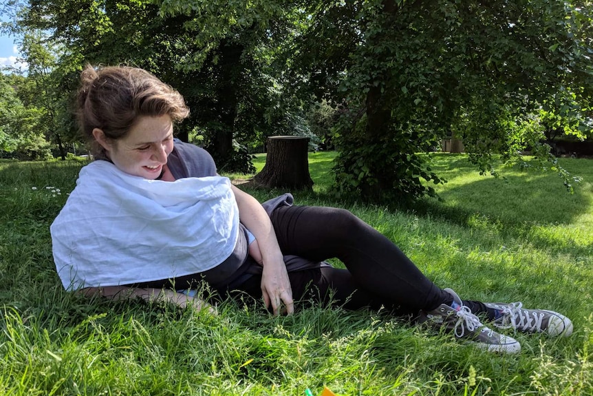 Olivia Humphreys lying on the grass outside with her baby, Kit.