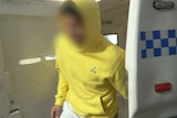 A man in a yellow hoodie in the back of a police car