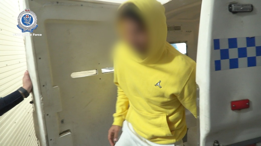A man in a yellow hoodie in the back of a police car